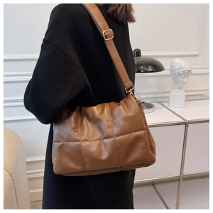 Sac bandoulière marron matelassé avec ferrures dorées porté par un mannequin en manteau noir