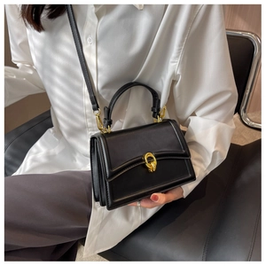 Detail of a black leather crossbody bag featuring a vintage gold twist-lock buckle closure