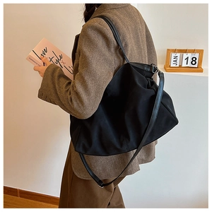 Detail of a large black nylon tote bag with leather straps on a brown plaid blazer