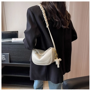 Detail of cream crossbody bag with woven strap and elephant charm on a shoulder