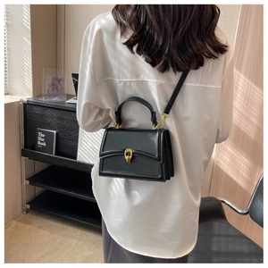 Detailed view of model wearing a black structured crossbody bag with gold hardware buckle