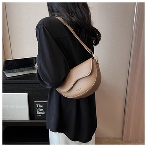 Classic brown leather saddle bag with wavy flap edge shown on desk with laptop