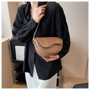 Brown leather saddle bag detail with curved flap and gold D-ring on female model