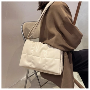 Détail du sac matelassé crème au fini brillant sur une tenue avec blazer marron