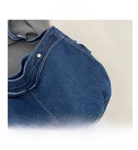 Close-up of denim messenger bag with white stitching and adjustable strap buckle