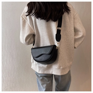 Rear view of a model wearing a black leather saddle crossbody bag with a wide nylon strap