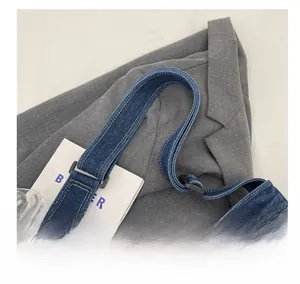 Detail of dark blue denim messenger bag with contrast stitching and adjustable buckle