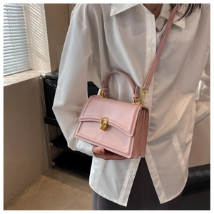 Detail of pink faux leather crossbody bag with iconic gold U-shaped metal buckle and handle