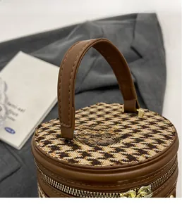 Close-up of houndstooth cylinder bucket bag with wide leather handle and gold zipper