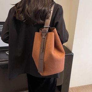 Sac seau minimaliste en cuir mat marron porté à l'épaule dans un décor intérieur