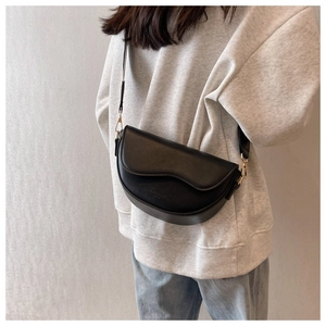 Side view of black crescent crossbody bag with adjustable gold buckle on grey sweater
