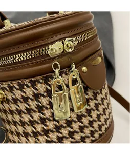 Detail of dual gold metal zippers on houndstooth bucket bag with leather trim and stitching