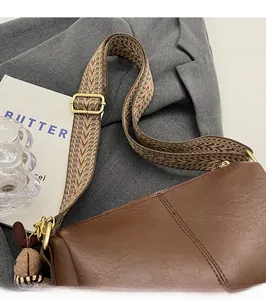 Brown leather handbag detail featuring a colorful woven strap and cute bear charm