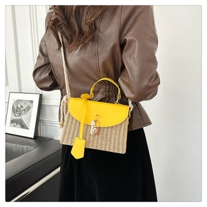 Détail d'un sac en paille avec rabat en cuir jaune et anse en corde sur modèle
