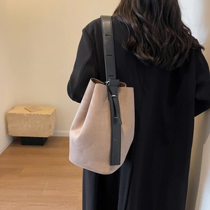 Sac seau minimaliste en daim beige mat avec une large bandoulière en cuir noir réglable