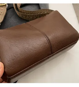 Detailed close-up of brown litchi grain leather crossbody bag with woven wide strap