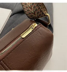Close-up of smooth gold metal zipper and colorful woven strap on brown leather bag