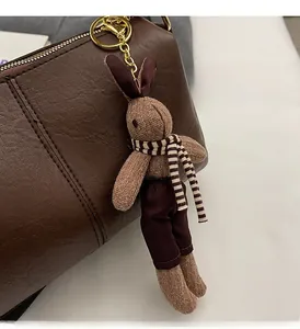 Close-up of a brown knitted rabbit charm with a striped scarf on a leather pillow bag