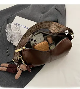 Interior view of brown cylinder bag showing capacity for phone and perfume with wide strap