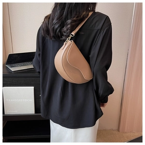 Brown leather saddle bag shown on model in a cozy indoor setting with a minimalist style