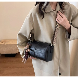 Détail d'un sac bandoulière cylindrique noir avec sangle large et pendentif ours