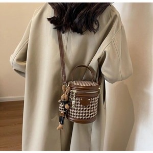 Detail of houndstooth cylinder bucket bag with a cute plush bunny charm and leather handle