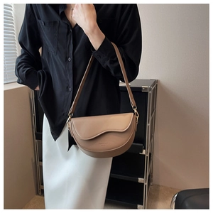 Detailed view of camel half-moon shoulder bag worn by model over black and white outfit