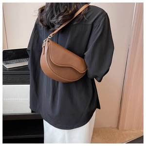 Brown faux leather saddle bag with wave edge flap shown on a model in a cozy setting