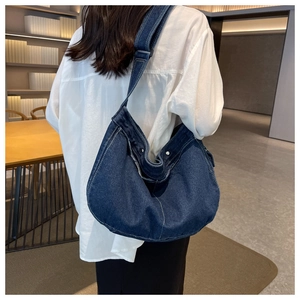 Detail view of large denim messenger bag featuring white stitching and silver snap button