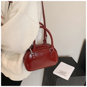 Detail of red patent leather Boston bag with silver hardware on a white sweater