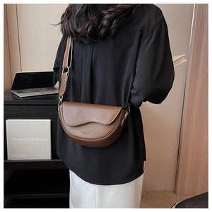 Brown leather saddle bag with wide strap worn by model in a modern office setting