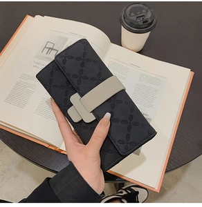 Vue détaillée d'un portefeuille noir à fleurs embossées et fermoir boucle sur un livre