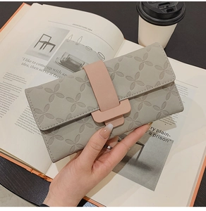 Portefeuille long gris gaufré avec boucle rose présenté dans un décor de style de vie