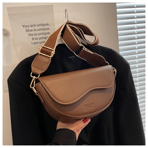 Detail of a vintage dark brown saddle bag with a wide patterned strap and gold hardware