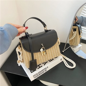 Sac à main en paille à la mode avec rabat en cuir noir et poignée en corde sur un livre