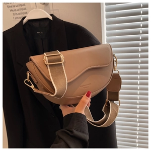 Detail of brown saddle bag with gold hardware and striped fabric shoulder strap