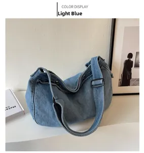 Close-up of light blue denim tote bag with adjustable black strap on white table