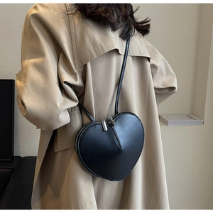 Dettaglio borsa a cuore in pelle nera abbinata a un trench beige dallo stile ricercato