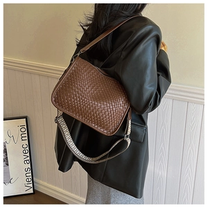 Detail of a brown woven shoulder bag featuring patterned and leather adjustable straps