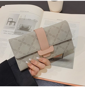 Vue détaillée du portefeuille gris en cuir avec trèfles embossés et bride rose contrastée