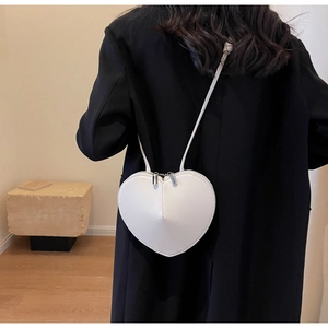 Dettaglio di una borsa a tracolla bianca a forma di cuore indossata su un blazer nero