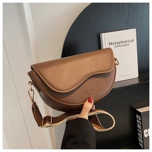 Detail of a brown saddle bag featuring a jacquard woven strap and gold hardware accents