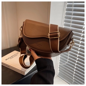 Close-up of brown saddle bag with adjustable wide strap and golden metal hardware