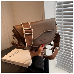 Detail of a brown leather saddle bag with wide woven strap and gold hardware accents