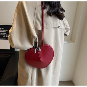 Dettaglio di una borsa a tracolla rossa a forma di cuore su un outfit trench beige