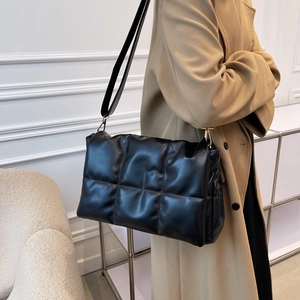 Sac bandoulière matelassé noir avec boucles dorées porté sur manteau en laine