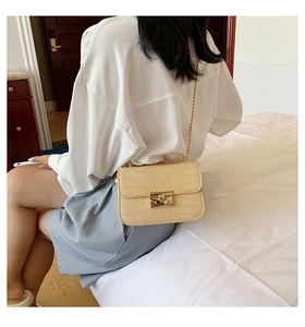 Close-up of beige crocodile pattern handbag featuring a gold chain and metal clasp