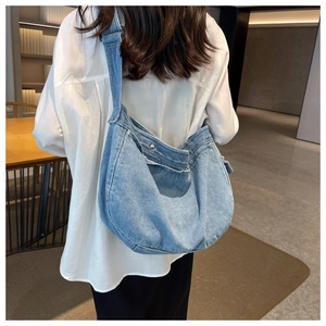 Side view of light blue denim messenger bag showing frayed edges and slouchy crescent shape