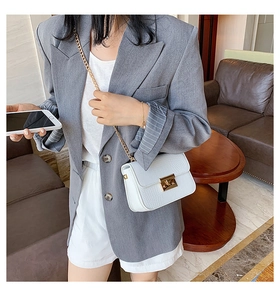 White faux crocodile skin crossbody bag with gold chain shown on a model in a grey suit