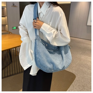 Detail of light blue denim crossbody bag featuring contrast stitching and wide strap